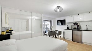 A modern hotel room with a bed, bedside tables, a desk, a chair, a dining table, and a kitchen area with a sink and appliances. - Appartement in the heart of Paris ☆ Opera ☆ (Paris)