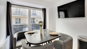 A modern dining area with a table set for two, a vase with flowers, and a view of a balcony with a railing. - Appartement in the heart of Paris ☆ Opera ☆ (Paris)