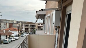 Een balkon met betegelde vloer, een metalen hekwerk en uitzicht op een straat met geparkeerde auto's.