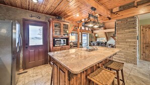 A spacious kitchen with a large island, wooden ceiling, and a stone accent wall. - Lakeside Haven with Sandy Beach, Sleeps 12, 3 Bath (Stigler)