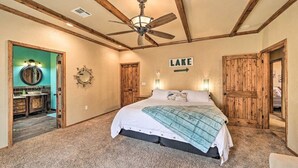 A bedroom with a bed, wooden ceiling beams, a ceiling fan, a sign indicating 'LAKE', and a bathroom visible through an open door. - Lakeside Haven with Sandy Beach, Sleeps 12, 3 Bath (Stigler)