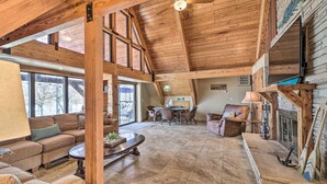 A spacious living area with a high ceiling, wooden beams, and a fireplace. There is a dining table with chairs and a sofa. - Lakeside Haven with Sandy Beach, Sleeps 12, 3 Bath (Stigler)