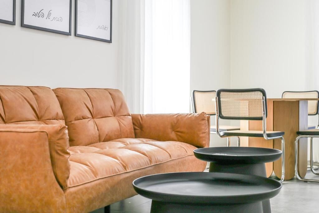Un salon moderne avec un canapé en cuir, une table à manger avec des chaises et des œuvres d’art encadrées accrochées au mur.
