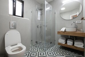 A bathroom with a toilet, a shower with glass doors, a sink with a mirror, and a patterned floor.