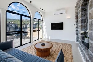 Una sala de estar moderna con ventanas amplias, una mesa de centro redonda y un televisor de pantalla plana montado en la pared.