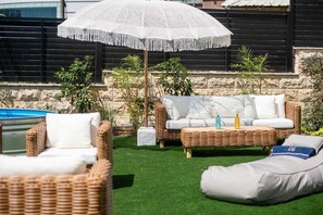 A patio area with wicker furniture, a white umbrella, and a pool.