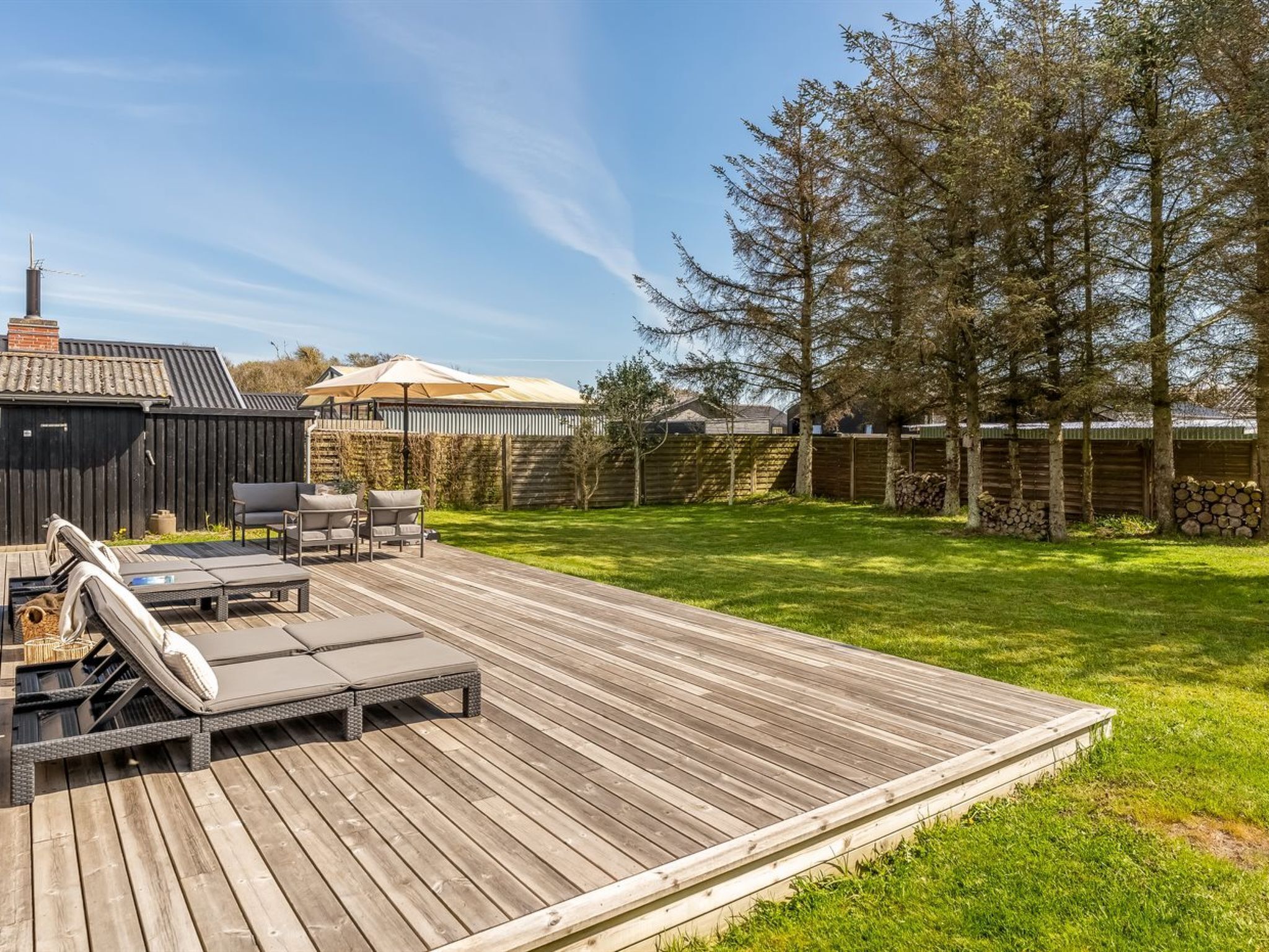 A wooden deck with outdoor furniture, a covered seating area, and a fenced yard with trees.