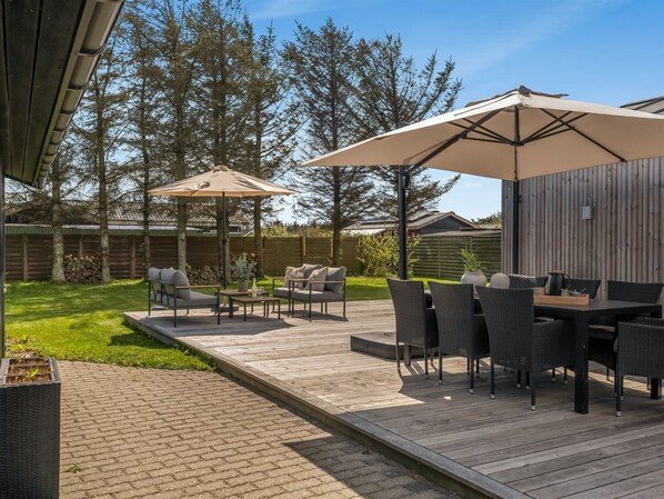 Un patio al aire libre con terraza de madera, mobiliario exterior y sombrillas.