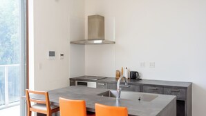 Una cocina moderna con una isla grande, dos sillas naranjas, una campana extractora de acero inoxidable y un ventanal que proporciona luz natural.