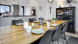 Una cocina moderna con armarios blancos, una mesa de comedor de madera y sillas negras. Hay lámparas colgantes esféricas sobre la mesa.