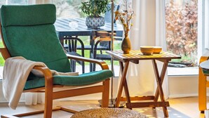A green chair with a woven ottoman, a small table with a vase and bowls, and a view of a balcony with plants. - "Henryette" - 1.5km from the sea by Interhome (Ebeltoft)