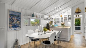 A modern kitchen with white cabinetry, a dining area with a round table and chairs, and a view of the outdoors through a window. - "Gonda" - 2km from the sea by Interhome (Saltum)