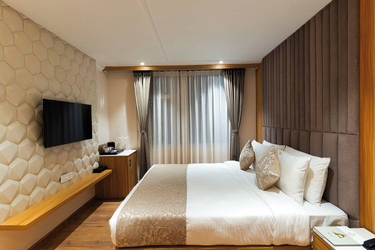 Una habitación de hotel moderna con una cama grande, un televisor de pantalla plana montado en una pared con diseño geométrico, una mesita de noche de madera y una ventana con cortinas.
