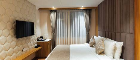 A modern hotel room with a large bed, a flat-screen TV mounted on a geometric-patterned wall, a wooden bedside table, and a window with curtains.