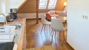 A modern kitchen with a built-in stove, a dining area with a table and chairs, and a loft bedroom with a sloped ceiling and skylights. - Sustainable, vegan-friendly accommodation at mining nature trail in Schneeberg (Schneeberg)