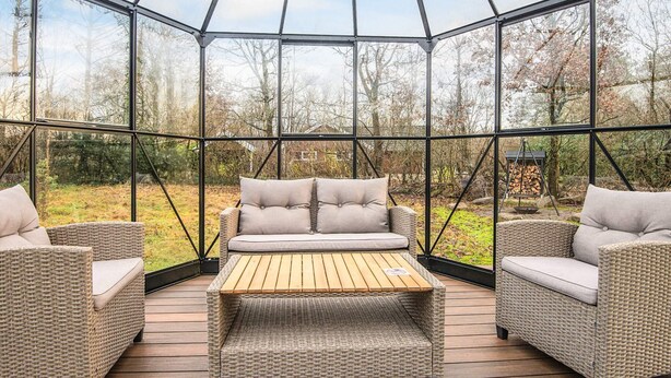 A glass-enclosed patio with wicker furniture and a wooden table. - 4 Person Holiday Home in Oksbol (Oksbol)
