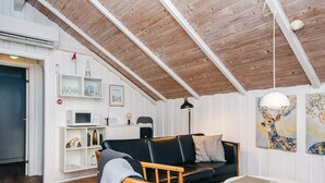 A cozy living room with a black leather sofa, wooden chair, and white round table. A bookshelf with various items and a painting of a deer are visible. - 4 Person Holiday Home in Oksbol (Oksbol)
