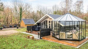 A modern house with a glass conservatory, a wooden deck, and outdoor seating. - 4 Person Holiday Home in Oksbol (Oksbol)