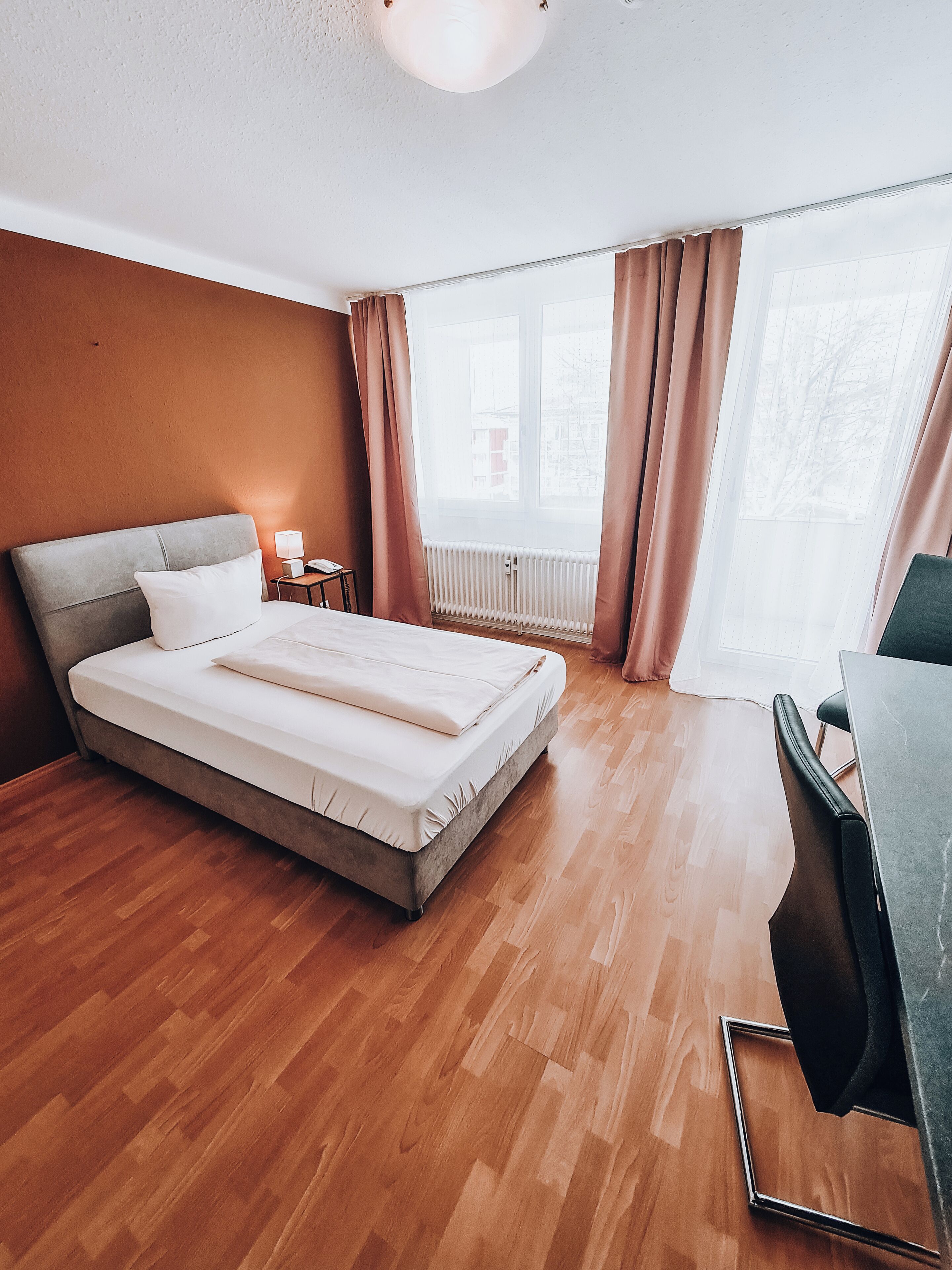 A hotel room with a bed, a desk, and a window with curtains.