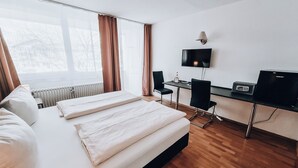 Ein Hotelzimmer mit einem Bett, einem Schreibtisch, einem Stuhl, einem Fernseher und einem fenster mit Vorhängen.
