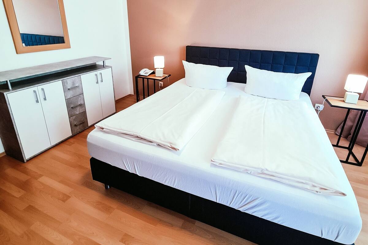 A neatly made bed with white linens, a dark headboard, and two bedside lamps.