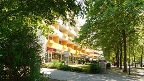 Ein modernes Gebäude mit gelber Fassade, einer überdachten Außenbereich-Sitzgelegenheit und einem Schild mit der Aufschrift 'Hotel Hallabonn'.