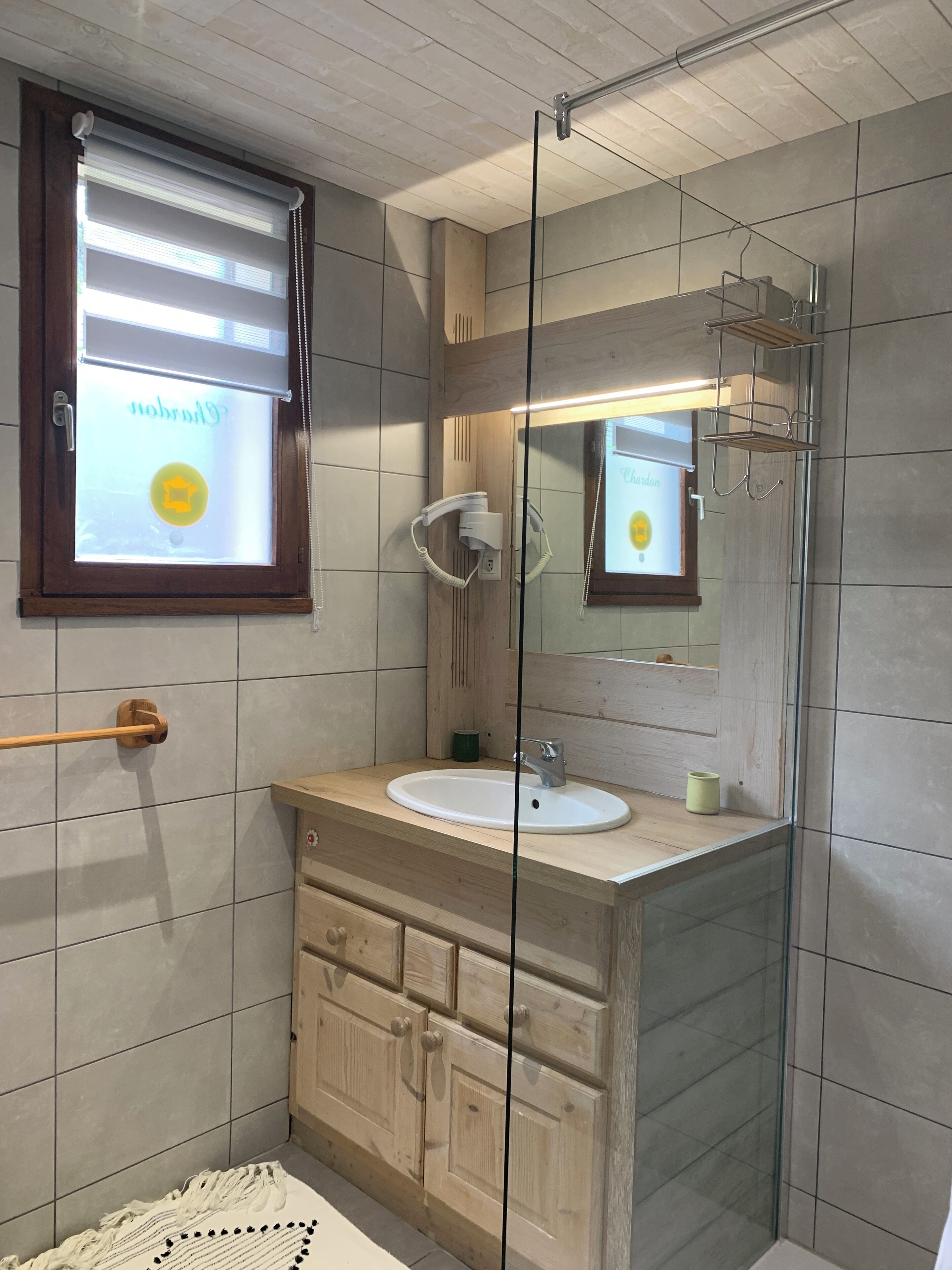 A bathroom with a wooden vanity, a glass shower enclosure, and a window with blinds.