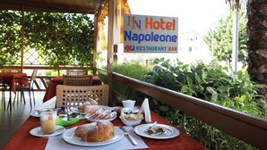 Una mesa de comedor con alimentos para el desayuno y un cartel del bar restaurante Hotel Napoleone.