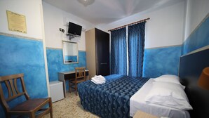 Habitación de hotel con cama, escritorio, silla, teléfono y televisión.