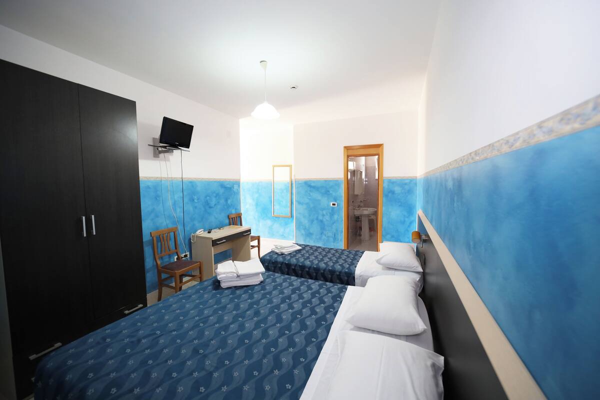 Hotellihuone, jossa on kaksi sänkyä, työpöytä, tuoli ja televisio.