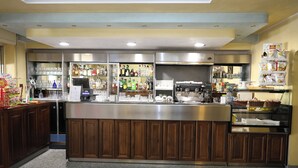 Zona de bar con mostrador de acero inoxidable, armarios de madera y una variedad de botellas y vasos.