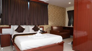 Ein Hotelzimmer mit einem großen Bett, einem hölzernen Kopfteil, einem braunen Ledersessel, einem Nachttisch aus Holz und einem Holzschrank.