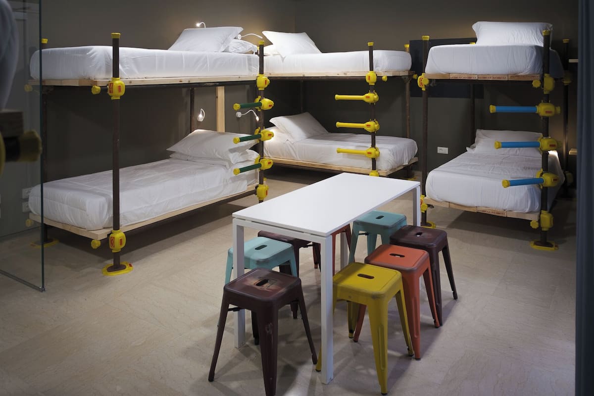 A bunk bed room with a white table and colorful stools.