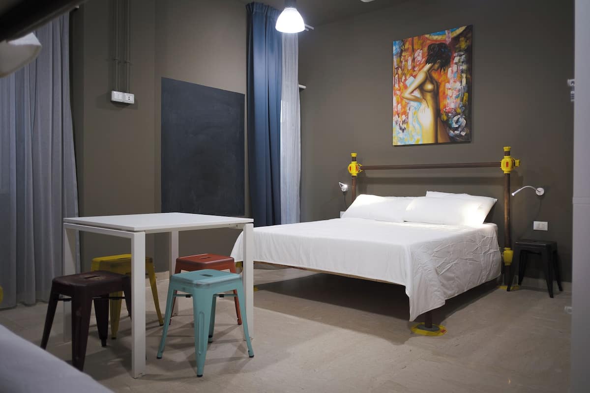 A bedroom with a bed, a desk, and two stools.