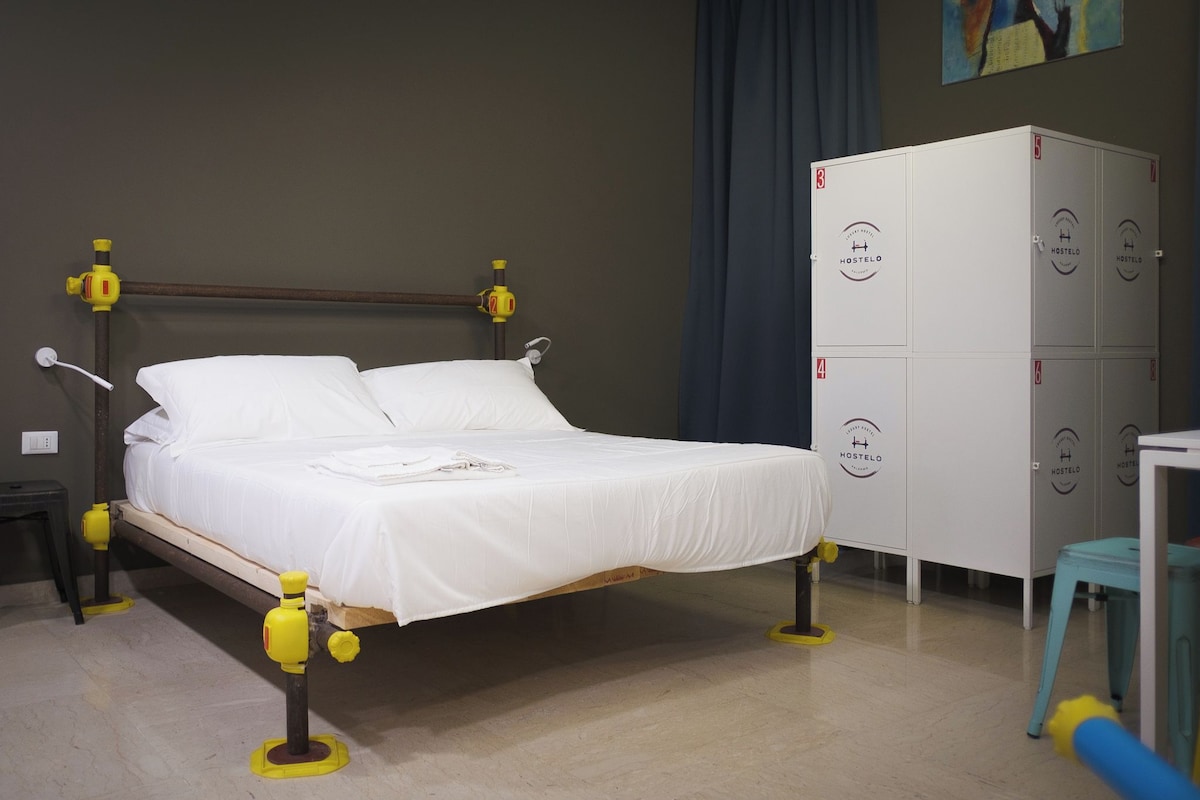 A bed with white bedding, a wooden headboard, and yellow safety railings. There is a white wardrobe with multiple compartments and a small blue stool.