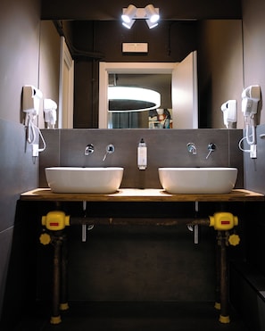 A modern bathroom with two sinks, a mirror, and hair dryers mounted on the wall. - Hostelò Luxury Hostel (Palermo)