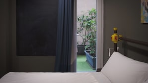 A hotel room with a bed, a window with curtains, a potted plant outside, and a yellow object on the wall. - Hostelò Luxury Hostel (Palermo)