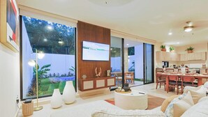 A modern living room with a flat-screen TV, a dining area with wooden furniture, and a kitchen with light-colored cabinets. - Palmara Gated Community, Pool, Paddle Court & Gym (Playa del Carmen)
