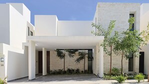 A modern building with a covered entrance, stone walls, and a small garden area. - Palmara Gated Community, Pool, Paddle Court & Gym (Playa del Carmen)