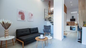 Una sala de estar moderna con un sofá, un sillón y una mesita. Se ve una escalera que sube a un nivel superior.