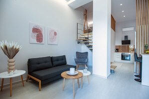 A modern living room with a sofa, a chair, and a small table. There is a staircase leading to an upper level.