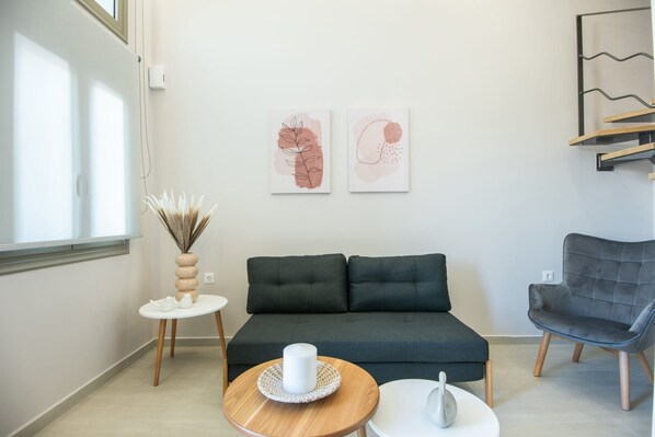 A modern living room with a dark green sofa, a grey armchair, a small round wooden table with a white candle, and two abstract paintings on the wall.