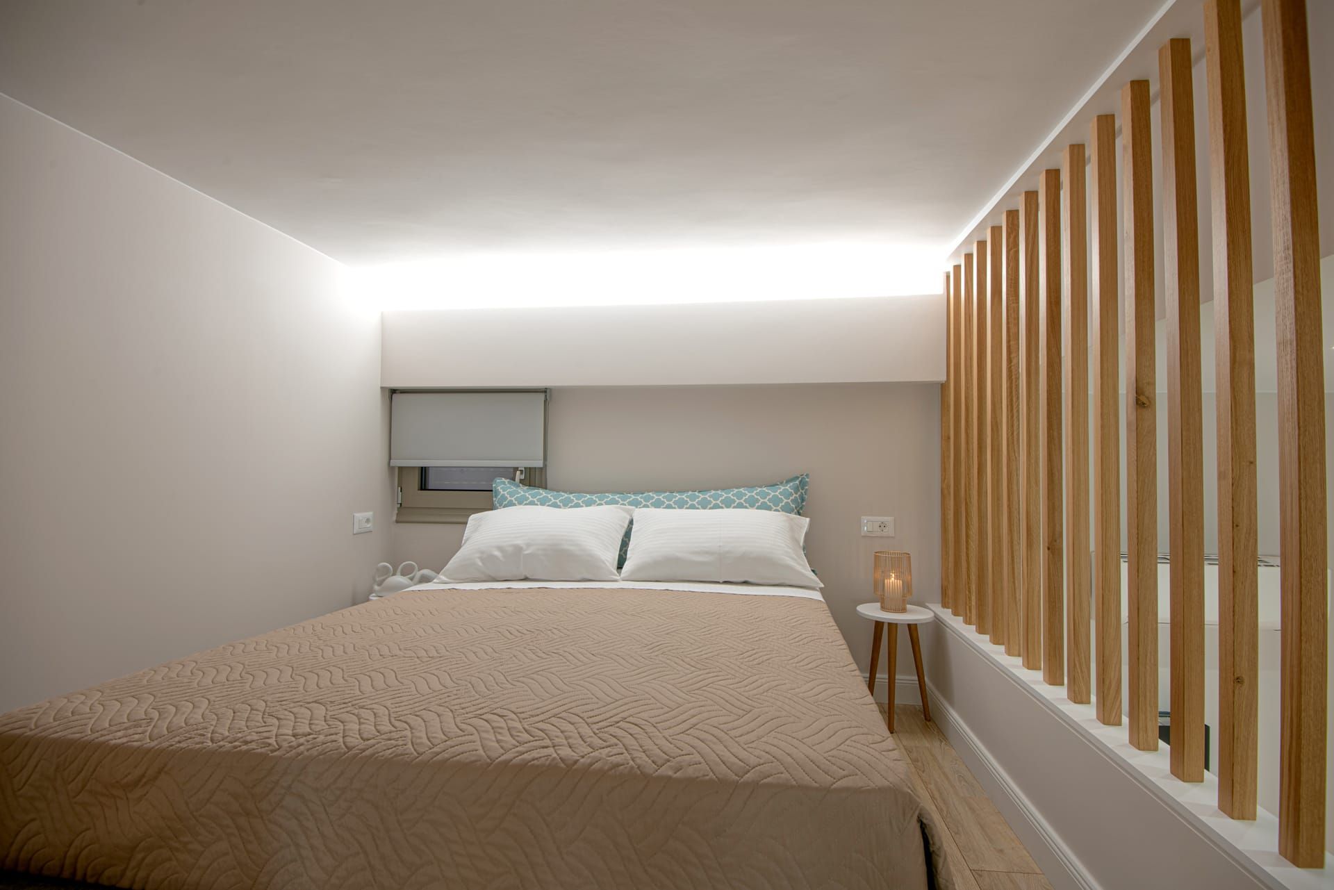 Un dormitorio con cama, mesita de noche, ventana con persianas y un separador de madera.