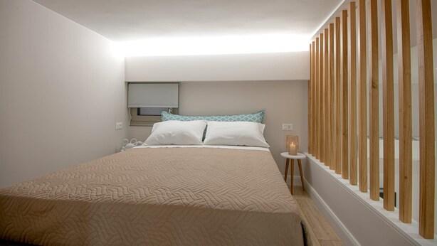 A bedroom with a bed, a bedside table, a window with blinds, and a wooden partition. - Mylos 2 apt, Apartment (Agios Nikolaos)