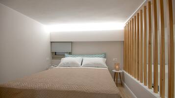 Un dormitorio con cama, mesita de noche, ventana con persianas y un separador de madera.
