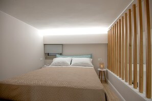 A bedroom with a bed, a bedside table, a window with blinds, and a wooden partition.