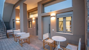 A modern outdoor seating area with tables and chairs, a staircase, and a large window. - Mylos 2 apt, Apartment (Agios Nikolaos)