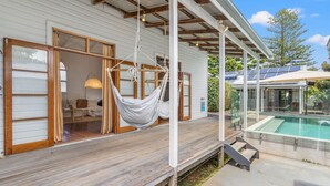 Una terraza de madera con una hamaca, una piscina y un porche cubierto.