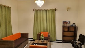 Una sala de estar con muebles de mimbre, una lámpara de araña y una cortina verde.