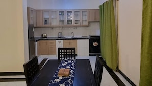 Un comedor con una mesa preparada para cuatro, una cocina al fondo y una cortina verde a la derecha.